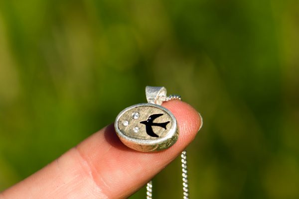 bird necklace on finger to show scale with green behind